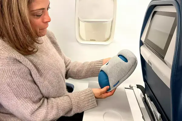 A person holding the Ostrichpillow Mini Handy Pillow on an airplane