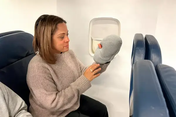A person holding the Ostrichpillow Mini Handy Pillow on an airplane