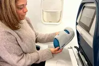 A person holding the Ostrichpillow Mini Handy Pillow on an airplane