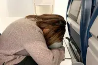 A person using the Ostrichpillow Mini Handy Pillow leaning forward on an airplane