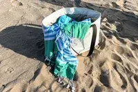 The Bay Laurel Turkish Beach Towel with Travel Bag draped in a bag on sand