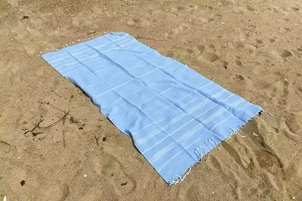 A blue Havluland Sultan Series Turkish Beach Towel on the sand