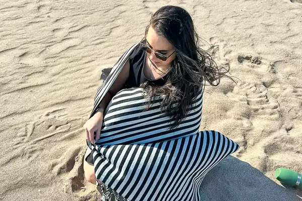 A person sitting on a beach wrapped up in the Fairmont Turkish Linen Towel