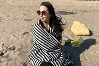 A person sitting on a beach wrapped up with the Fairmont Turkish Linen Towel