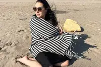 A person sitting on a beach wrapped up in the Fairmont Turkish Linen Towel