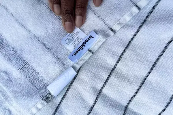 A persons hand touching the tag on the Brooklinen Turkish Flatweave Beach Blanket