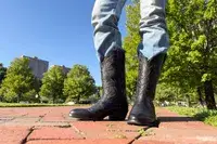 A person wears the Ariat Heritage R Toe Western Boots outside