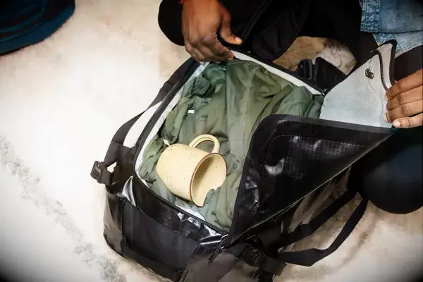 Hands holding open the Patagonia Black Hole 40L Duffel Bag packed with a jacket and mug