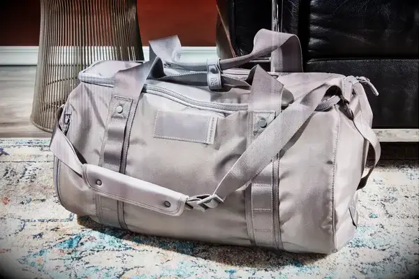 A duffel bag on a patterned rug with furniture in the background