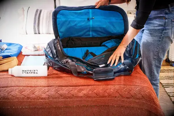 a person opening an empty Gregory Alpaca Duffel 60 on a bed