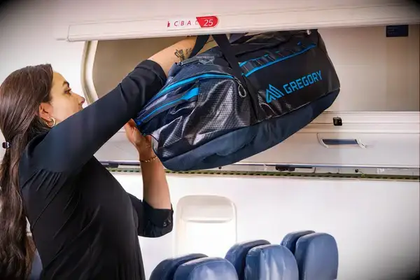 A person placing the Gregory Alpaca Duffel 60 into an overhead compartment on an airplane