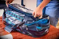 A person zipping up the Gregory Alpaca Duffel 60 on a bed