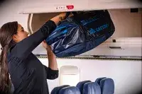 A person placing the Gregory Alpaca Duffel 60 into an overhead compartment on an airplane
