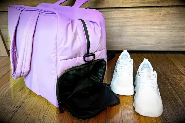 Calpak Luka Large Duffel with the shoe compartment open next to a pair of sneakers