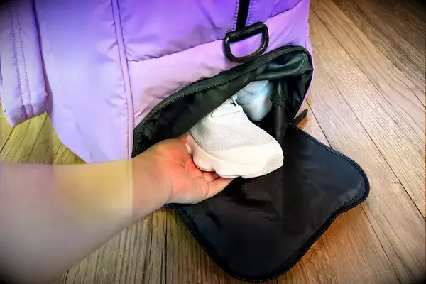 A hand grabbing a shoe out of the Calpak Luka Large Duffel shoe compartment