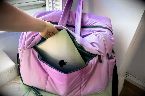 A hand placing a laptop in the pocket of the Calpak Luka Large Duffel