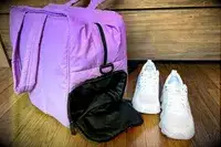 Calpak Luka Large Duffel with the shoe compartment open next to a pair of sneakers