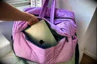 A hand placing a laptop in the pocket of the Calpak Luka Large Duffel