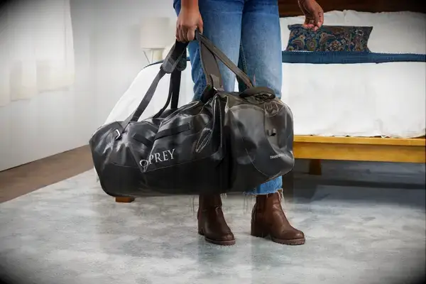 A person holds the Osprey Transporter Waterproof Duffel 70L by the top handles