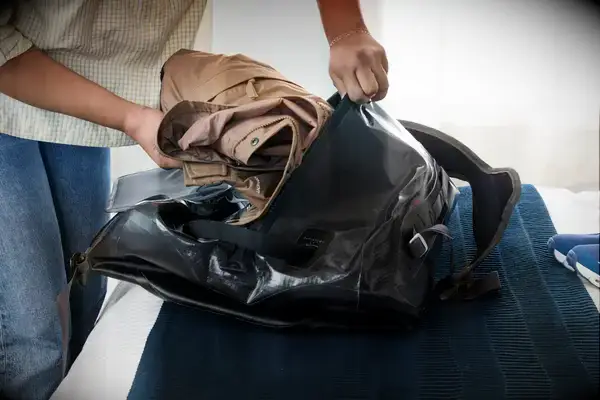 A person packs clothing into the Osprey Transporter Waterproof Duffel 70L