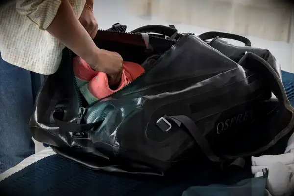 A person places shoes into the Osprey Transporter Waterproof Duffel 70L