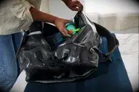 A person places a water bottle into the Osprey Transporter Waterproof Duffel 70L