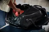 A person places shoes into the Osprey Transporter Waterproof Duffel 70L