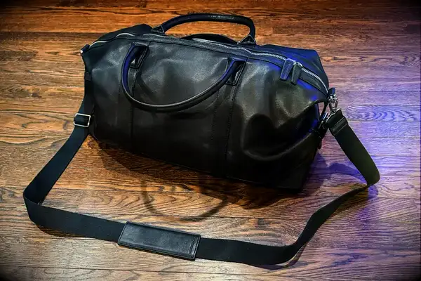A Leatherology Kessler Medium Duffle with a strap resting on a wooden floor