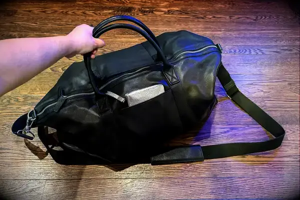 Hand holding a Leatherology Kessler Medium Duffle bag wallet visible in side pocket