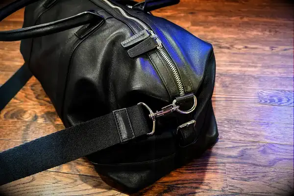 Black leather duffel bag with a zipper and strap detail on a wooden floor