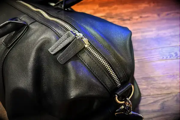 Closeup of a leather bag with a zipper and metal accents placed on a wooden surface