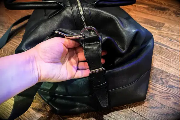 A hand adjusting a strap buckle on a Leatherology Kessler Medium Duffle