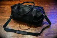 A Leatherology Kessler Medium Duffle with a strap resting on a wooden floor