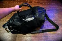 Hand holding a Leatherology Kessler Medium Duffle bag wallet visible in side pocket