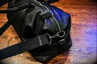 Black leather duffel bag with a zipper and strap detail on a wooden floor