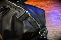 Closeup of a leather bag with a zipper and metal accents placed on a wooden surface