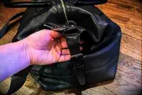 A hand adjusting a strap buckle on a Leatherology Kessler Medium Duffle
