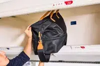 A person places the Mark & Graham Terminal 1 Expandable Travel Tote into an overhead compartment