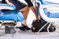 A person places the Mark & Graham Terminal 1 Expandable Travel Tote under the seat in front of them