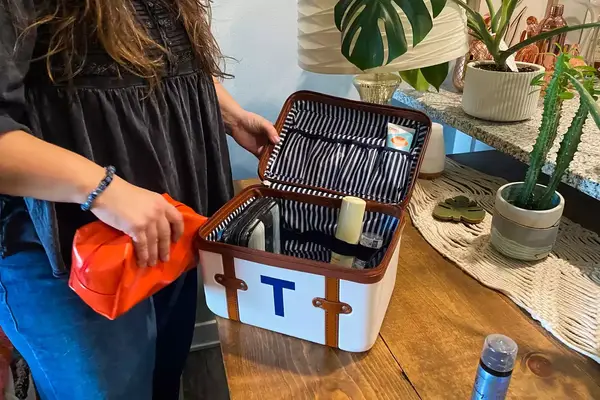A person places toiletry items into the Mark & Graham Terminal 1 Cosmetic Case