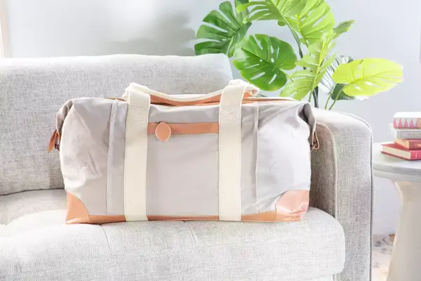 Mark & Graham Canvas and Leather Weekender on a grey couch next to a plant