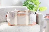 Mark & Graham Canvas and Leather Weekender on a grey couch next to a plant