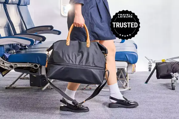 Someone walks down an airplane aisle holding a bag