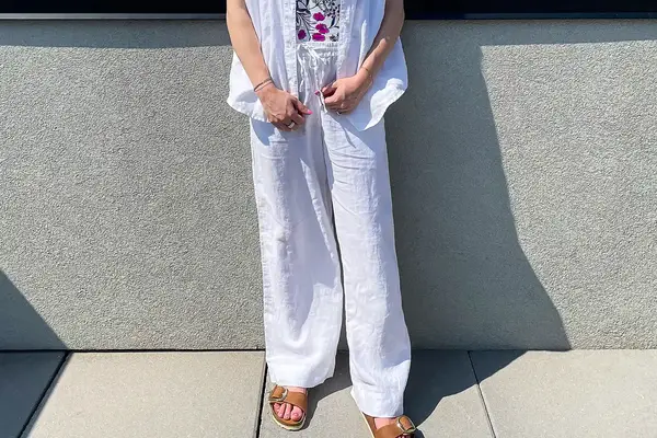 A person wearing a white outfit and sandals standing outdoors against a wall