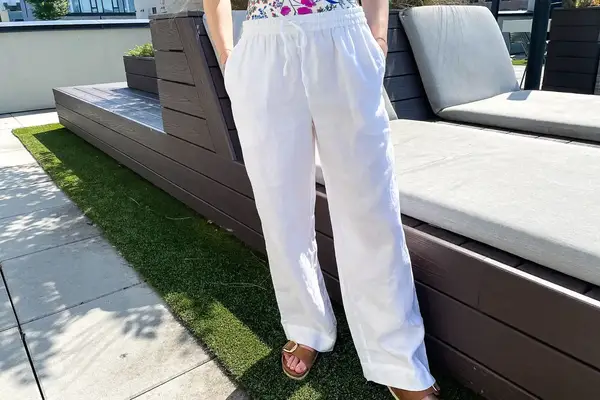 A person wearing Tommy Bahama Two Palms High-Rise Linen Easy Pants and sandals standing on outdoor flooring alongside seating