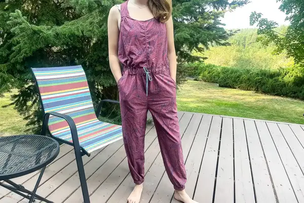 A person wearing a jumpsuit standing near a chair and a table on a wooden deck outdoors
