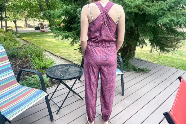 Back view of a person standing outdoors on a deck in a jumpsuit with a garden in the background