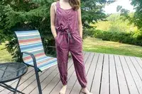 A person wearing a jumpsuit standing near a chair and a table on a wooden deck outdoors