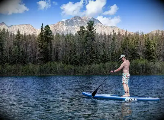 A person standing on the Atoll 11-foot Inflatable Stand-up Paddle Board while paddling on a lake