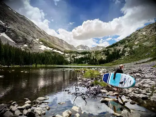 A person carrying the inflated Isle Pioneer 2.0 Paddle Board across rocks on the shore